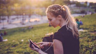 Stock Image: An athlete sits in the park typing on her smartphone