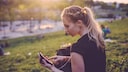 Stock Image: An athlete sits in the park typing on her smartphone