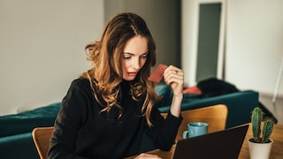 A woman sits at her laptop with her credit card ready.