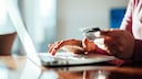 Person sitting at laptop with credit card in hand