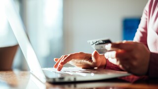 Person sitting at laptop with credit card in hand