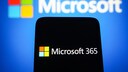 Microsoft 365 on a cell phone, with the Microsoft logo behind it