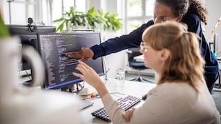 Two women at the PC with code in front of them perhaps from password managers