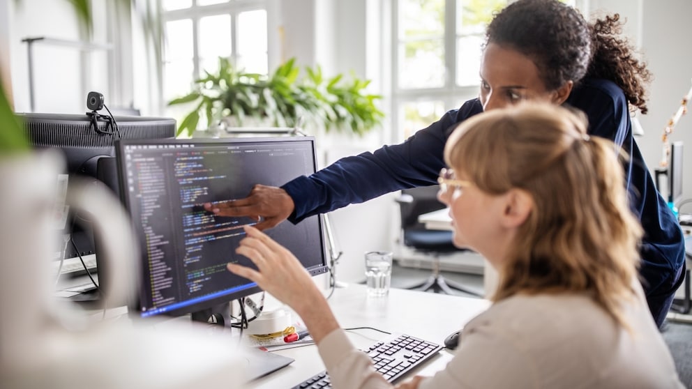 Two women at the PC with code in front of them perhaps from password managers