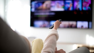 Person sits on the sofa and points to the TV with the remote control