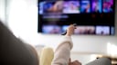 Person sits on the sofa and points to the TV with the remote control