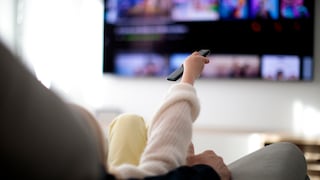 Person sits on the sofa and points to the TV with the remote control