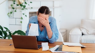 Woman touches her head while sitting in front of the computer with bills