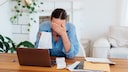 Woman touches her head while sitting in front of the computer with bills