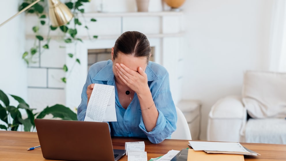 Woman touches her head while sitting in front of the computer with bills