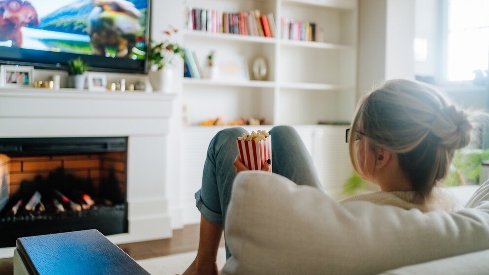 Woman sits on the sofa with popcorn and watches TV