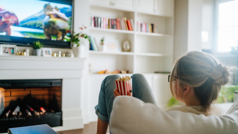 Woman sits on the sofa with popcorn and watches TV