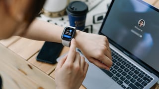 Smartwatch on wrist with laptop in the background