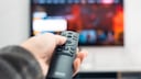 Person holds remote control pointed at TV