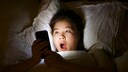 A girl lies in bed, looking startled at her smartphone.