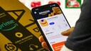 Person holds an Amazon package in one hand and has the Amazon app open on their smartphone.