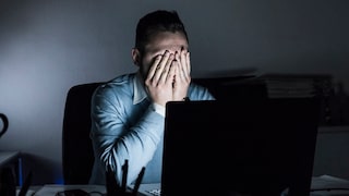 Man Covers His Face With His Hands in Front of Laptop