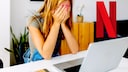 Woman sits in front of a laptop and covers her face with her hands