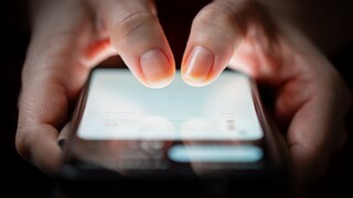 Close-up of a woman's thumbs touching a smartphone screen in the dark.