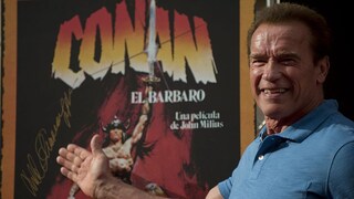 Arnold Schwarzenegger in front of a "Conan" poster