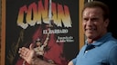 Arnold Schwarzenegger in front of a "Conan" poster