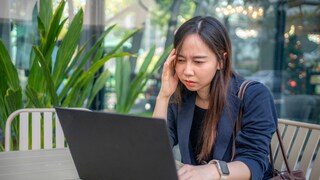 Woman with a stressed expression sits in front of a laptop