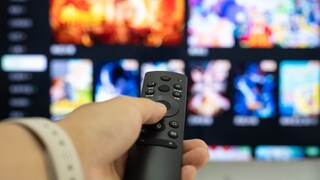 Hand holding the TV remote with a television in the background