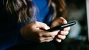 Woman in a blue T-shirt and black blazer looks at her smartphone