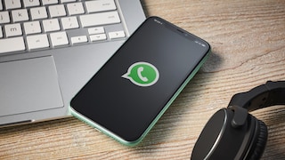 Smartphone with WhatsApp logo next to laptop and headphones
