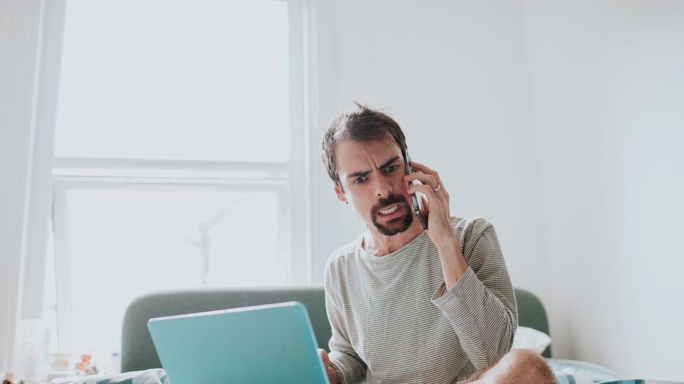 An angry man on the phone, a laptop in front of him