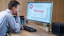 Man in front of a computer displaying a warning.