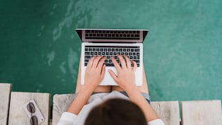 Woman Sits on Dock With Feet in Water and Laptop on Lap