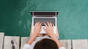 Woman Sits on Dock With Feet in Water and Laptop on Lap