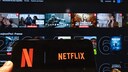 Smartphone with a large Netflix logo on the display. In the blurred background, various movie and series covers are visible.