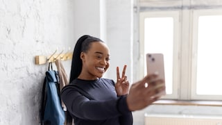 Young dark-skinned woman taking a selfie and flashing the peace sign.