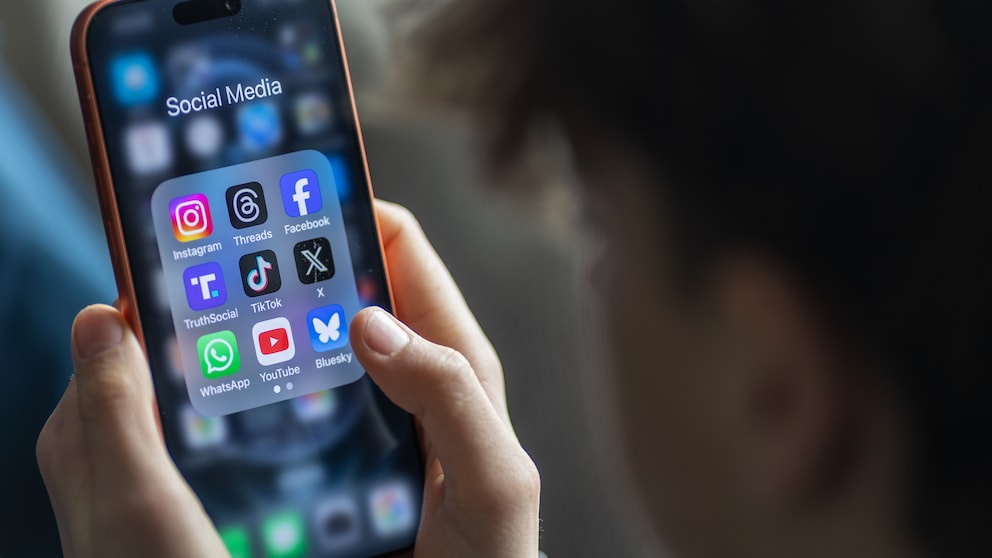 Teenager holds a smartphone displaying numerous social media apps.