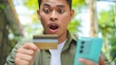 Man Looks Shocked at Credit Card and Smartphone
