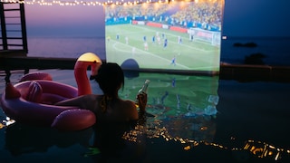 Person in Pool Watches Soccer on Big Screen