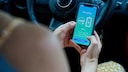 A person holds a smartphone in a car, displaying the charging process of an electric vehicle.