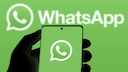 A person holds a smartphone displaying a green screen with the WhatsApp logo. The background is the same green with a second WhatsApp logo.