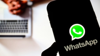 Smartphone with WhatsApp logo in the foreground, a person on a laptop in the background.