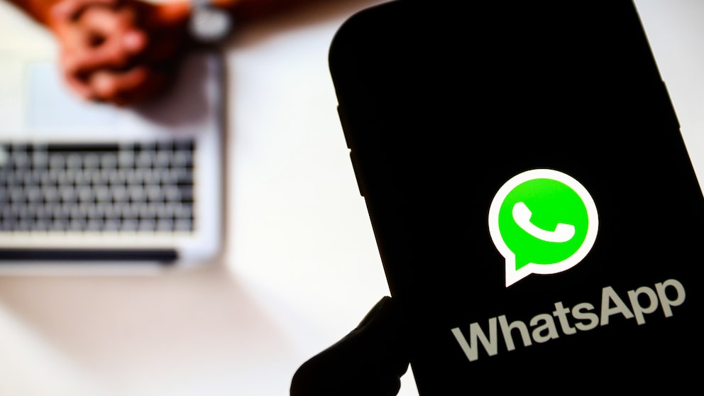 Smartphone with WhatsApp logo in the foreground, a person on a laptop in the background.