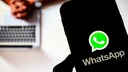 Smartphone with WhatsApp logo in the foreground, a person on a laptop in the background.