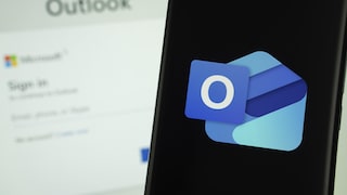 Outlook logo on a smartphone, with the Outlook login screen in the background on a computer