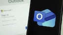 Outlook logo on a smartphone, with the Outlook login screen in the background on a computer