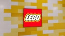 A red Lego logo appears on a rectangular screen in front of a wall made of staggered yellow and white rectangular elements. The logo is centered in the image and surrounded by a black frame. The design of the background wall resembles stacked Lego bricks.