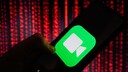 A hand holds a smartphone displaying a large FaceTime icon on the screen. In the background, blurred red light patterns evoke the appearance of digital data streams.
