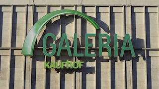 Green Galeria Kaufhof logo on a light stone or concrete facade with vertical structures and visible shadows