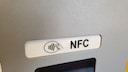 Close-up of an NFC symbol with the inscription "NFC" on a card reader or ATM. Below the symbol, part of the display is visible.