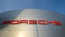 Porsche logo in red letters on a silver building facade, captured from a low angle against a blue sky.